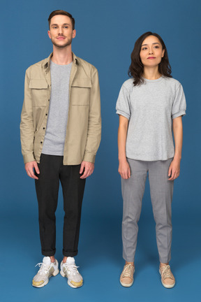 Young man and woman standing still in front of camera