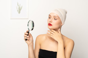 Young woman looking through magnifier and touching her chin