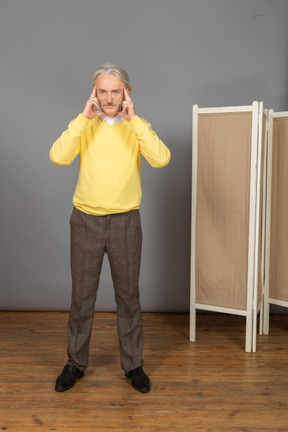 Vista frontal de un anciano concentrado tocando sus sienes mientras mira a la cámara