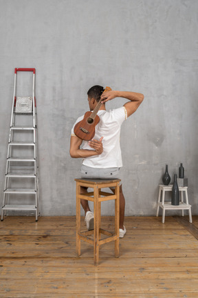 Back view of a man on a stool holding a ukulele behind his back