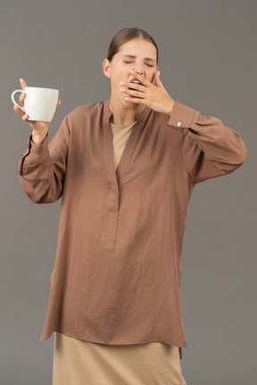 Mujer joven bostezando con taza de café