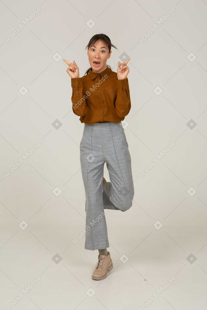 Vista frontal de uma jovem mulher asiática de calça e blusa, levantando as mãos