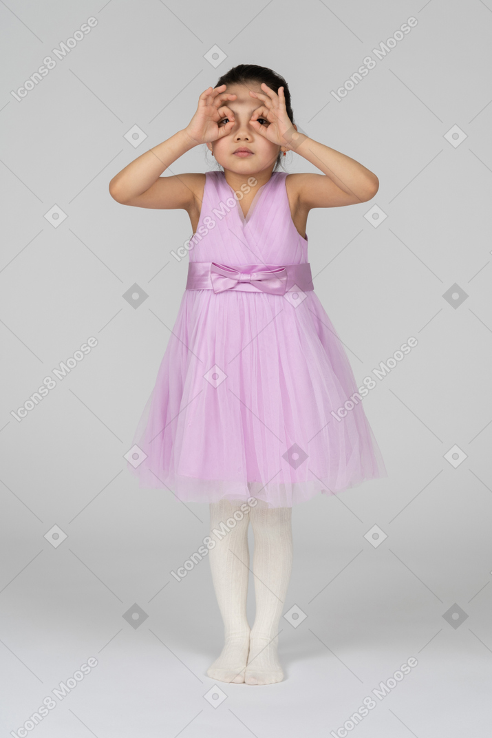 穿粉色连衣裙的小女孩透过手指面具看