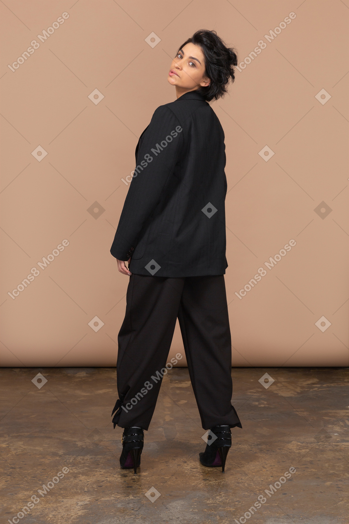 Vista posterior de una joven empresaria en un traje negro dándose la vuelta y mordiendo los labios