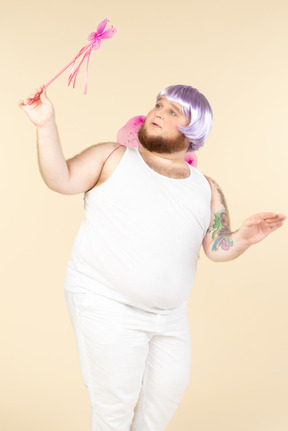 Young overweight man dressed as a fairy holding fairy wand and looking aside