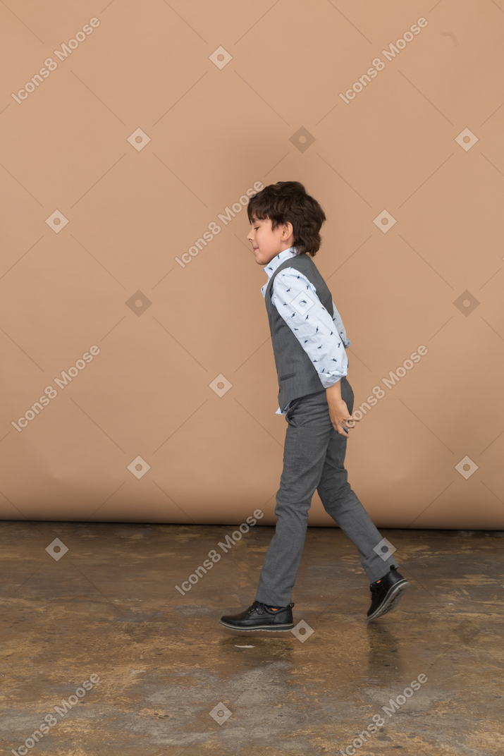 Вид сбоку мальчика в сером костюме, идущего