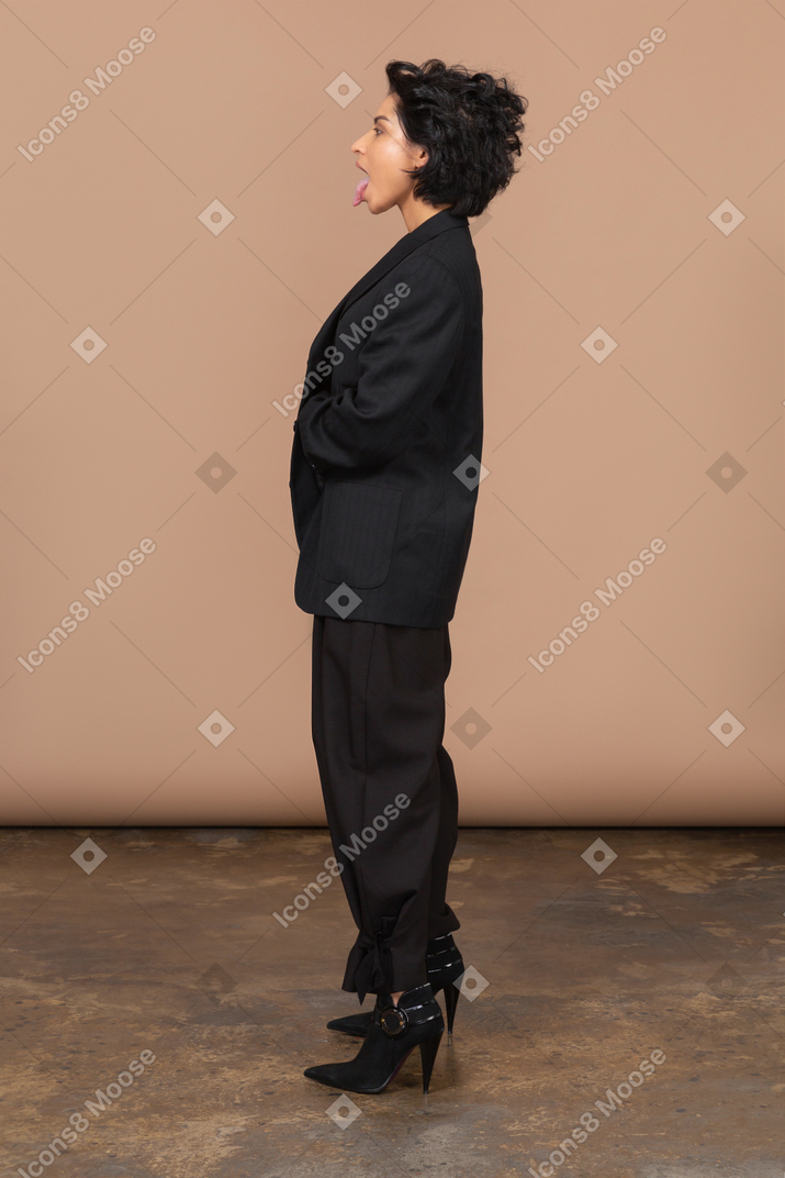 Seitenansicht einer geschäftsfrau, die schwarzen anzug trägt und zunge zeigt