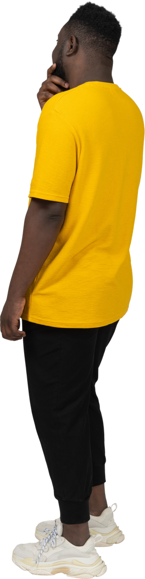Vista traseira a três quartos de um jovem adivinhando homem de pele escura em uma camiseta amarela tocando o queixo