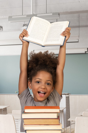 A young girl holding up a book in a classroom