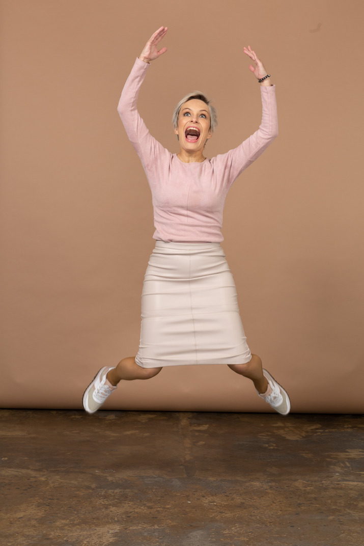 Front view of an emotional woman in casual clothes jumping with raised arms