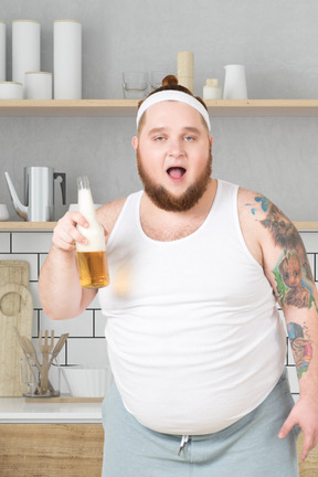 Homem parado na cozinha com uma garrafa de cerveja