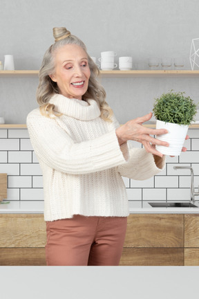 A woman holding a potted plant in her kitchen