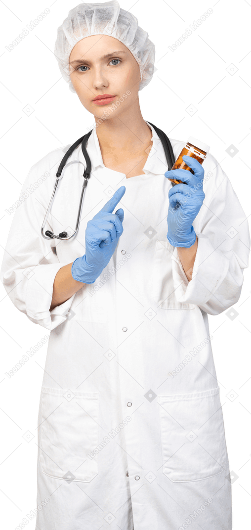Vista frontal de una joven doctora señalando con el dedo el frasco de pastillas