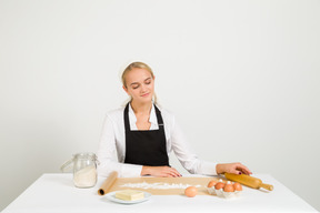 Chef mujer sentada en la mesa con ingredientes de pastelería en ella