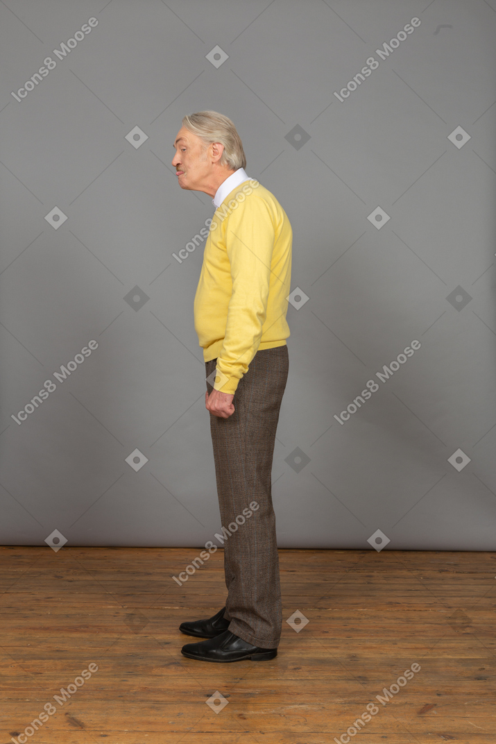 Side view of an old man in a yellow pullover bending down and showing tongue