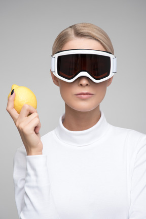 Young blonde woman in ski goggles holding lemon