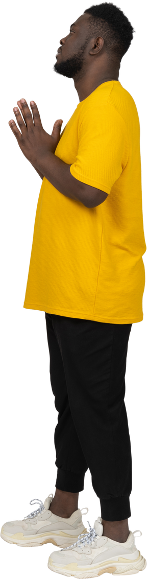 Vista laterale di un giovane uomo dalla pelle scura in maglietta gialla che si tiene per mano insieme