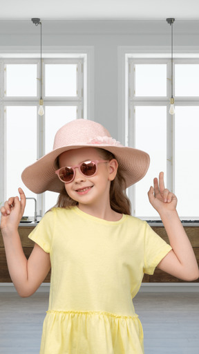 A girl wearing a hat and sunglasses stands in front of a window
