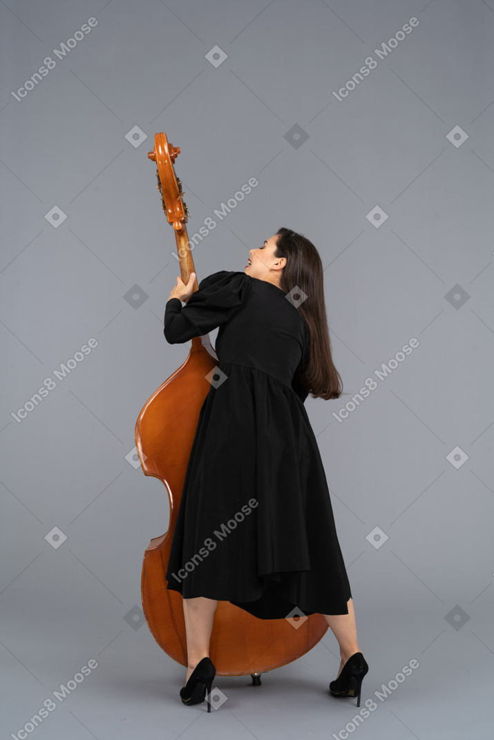 Vista posterior de un joven músico en vestido negro sosteniendo su contrabajo
