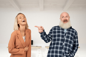 Smiling old man pointing at laughing young female colleague