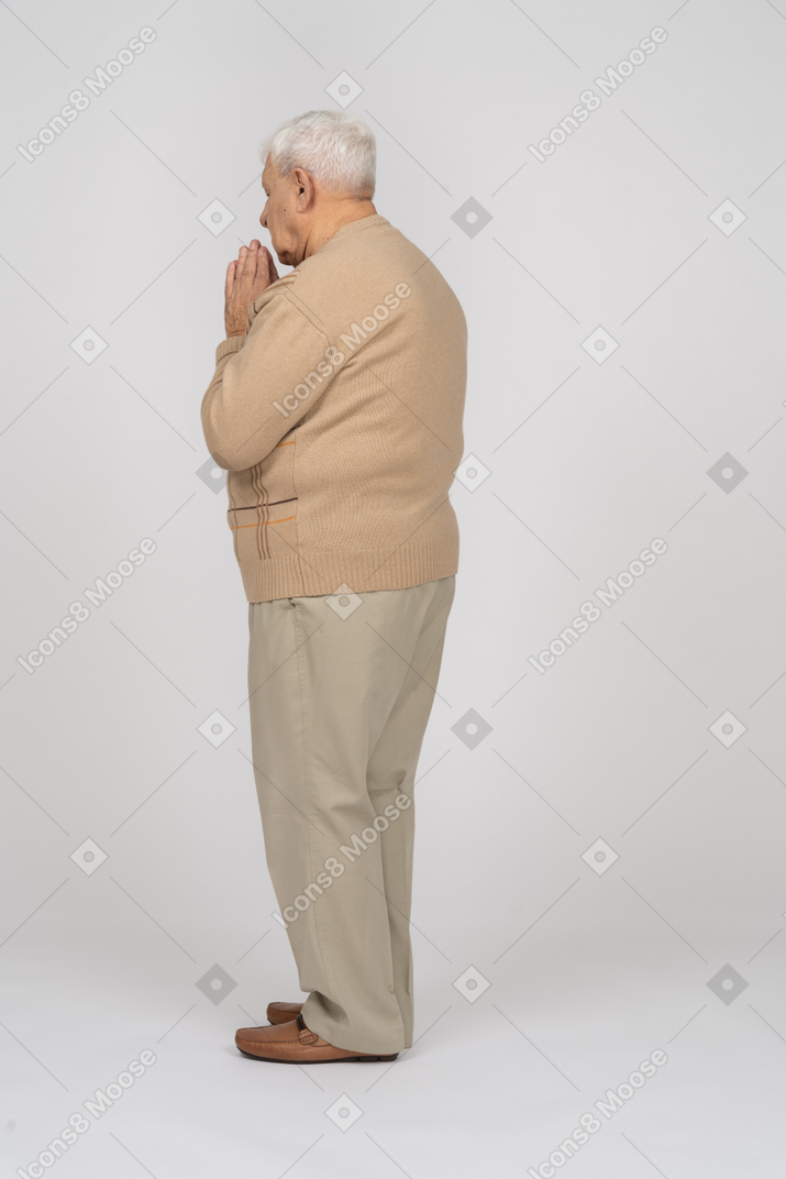 Vista lateral de un anciano con ropa informal se toma de la mano en gesto de oración
