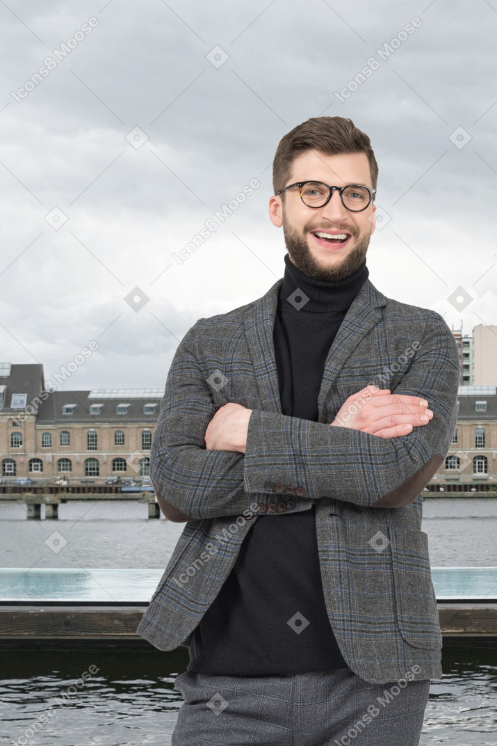 A man with a beard and glasses standing in front of a body of water