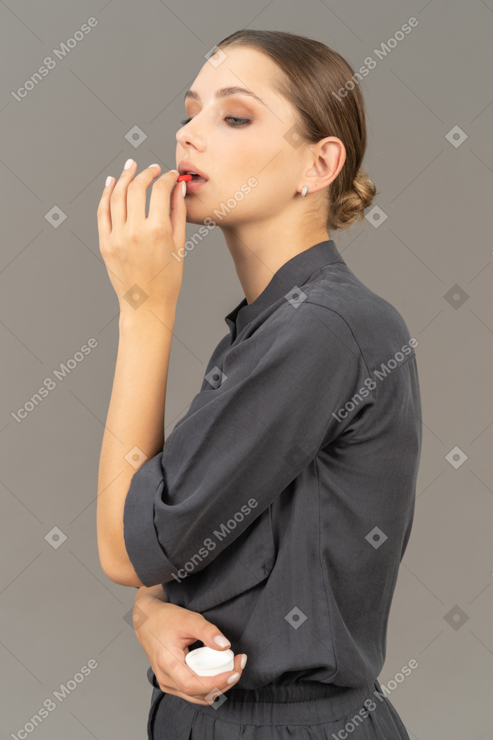 Vista de tres cuartos de una mujer joven en un mono tomando píldora