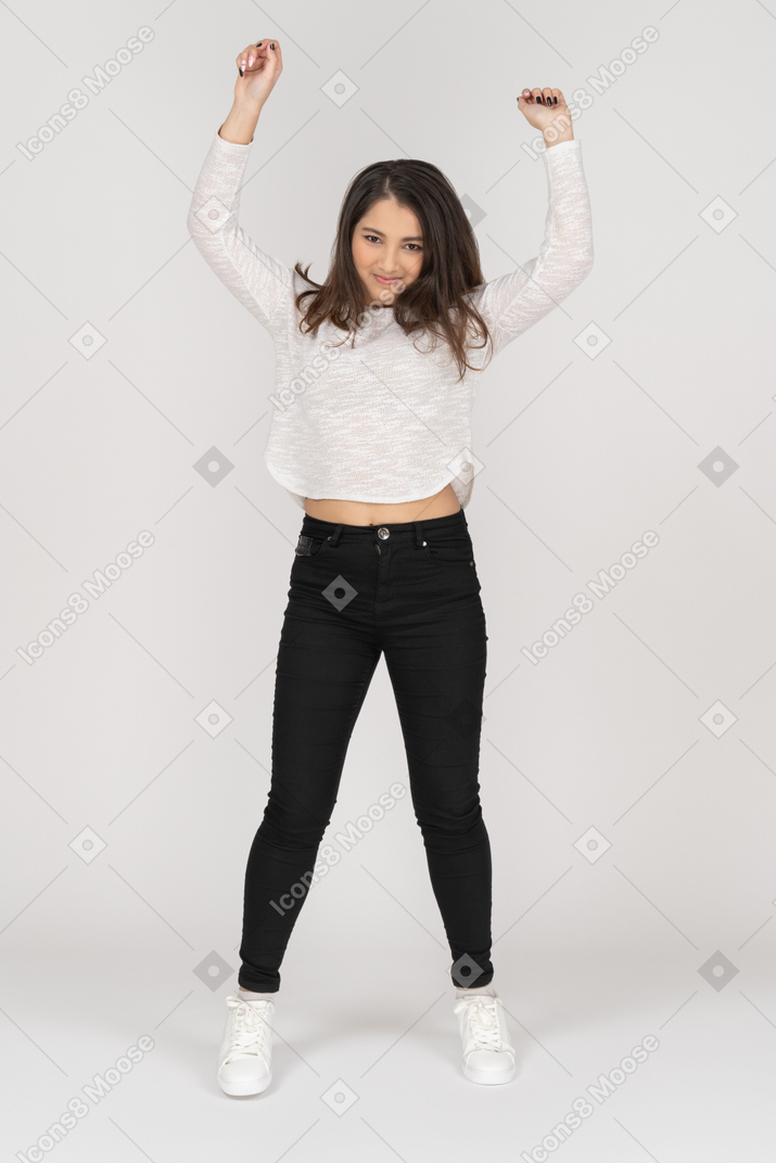 Front view of a young dancing indian female in casual clothes raising hands