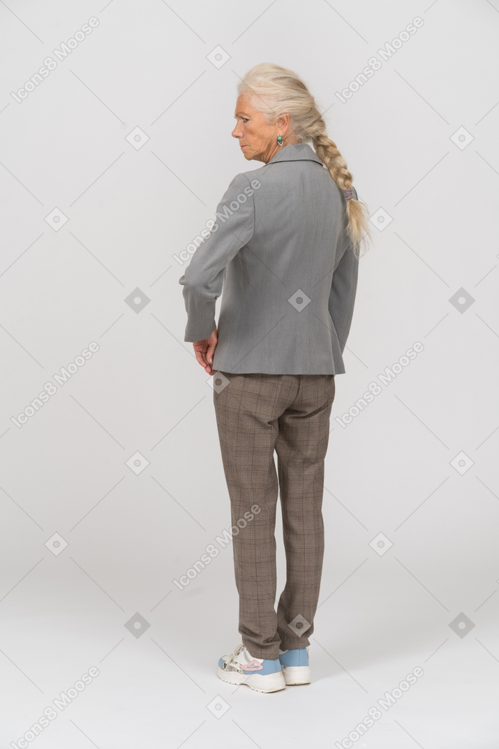 Vue arrière d'une vieille femme en costume posant avec la main sur la hanche