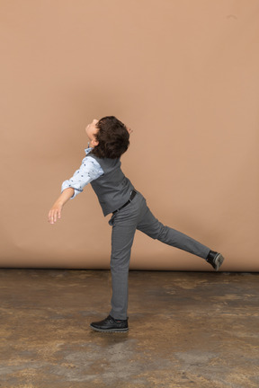 Vista lateral de um menino de terno equilibrando em uma perna com os braços estendidos