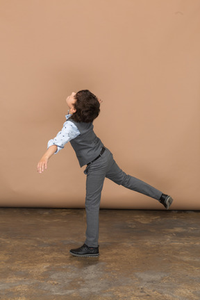 Vista lateral de un niño en traje de equilibrio sobre una pierna con los brazos extendidos