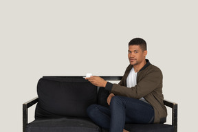 一个年轻人坐在沙发上，拿着一杯咖啡的前视图