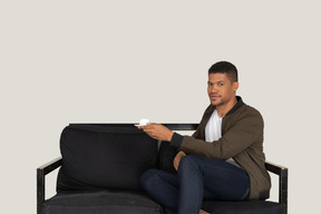 Front view of a young man sitting on a sofa with a cup of coffee