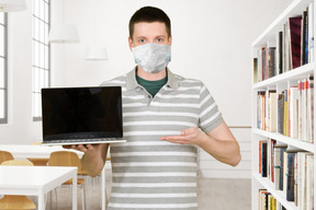 A man wearing a face mask holding a laptop