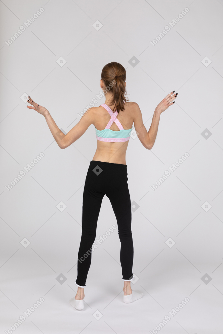 Вид сзади девушки-подростка в спортивной одежде, поднимающей руки и танцующей
