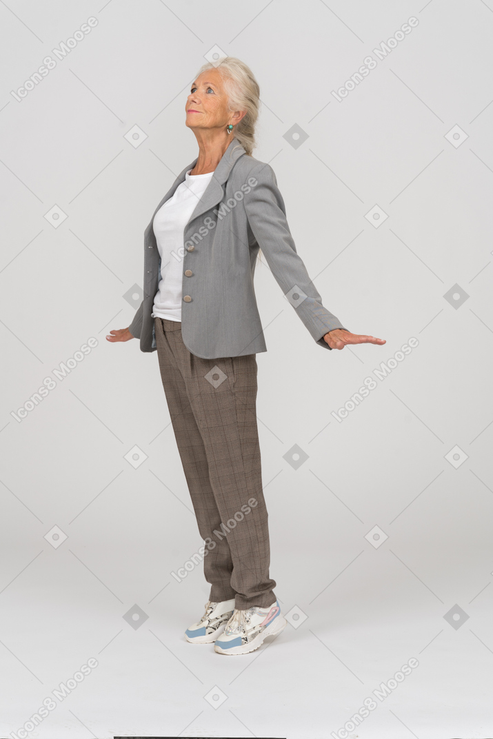 Side view of an old lady in suit standing on toes and outstretching arms