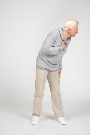 Front view of a man bending down with hand on his chest and looking away