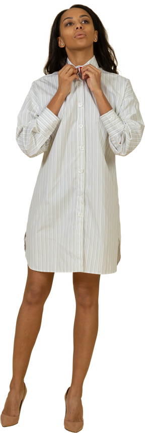 Vista frontal de una mujer joven de piel oscura con vestido blanco ajustando su cuello