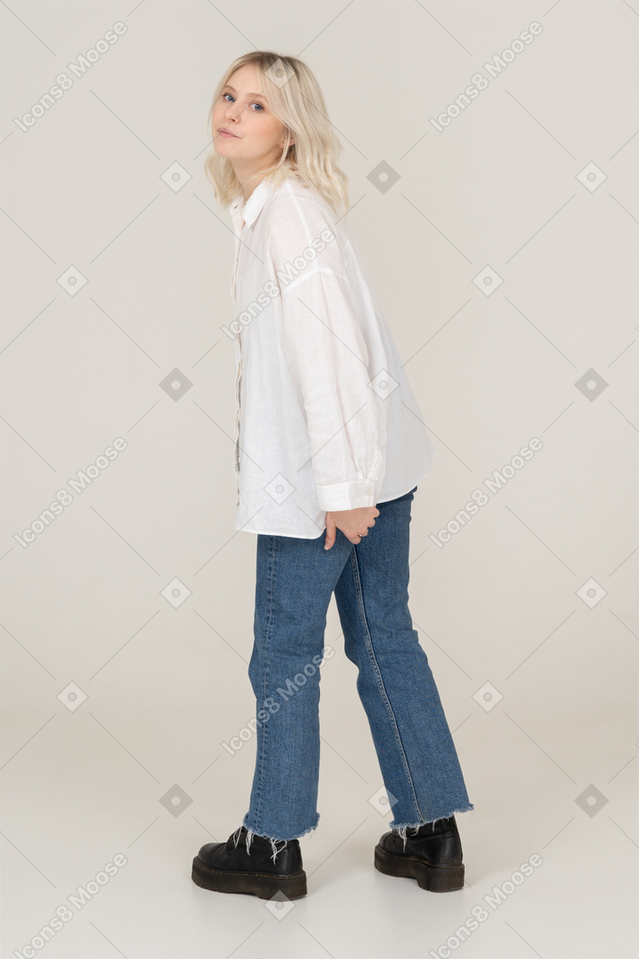 Vista lateral de una mujer rubia en ropa casual caminando y mirando a la cámara