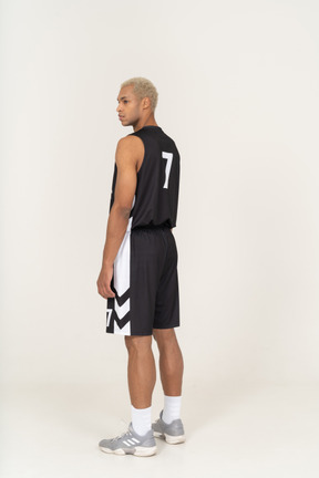 Three-quarter back view of a young male basketball player standing still & looking aside