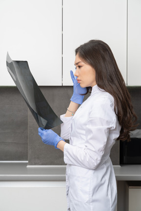 Side view of a young female doctor looking at an x-ray image and touching her head