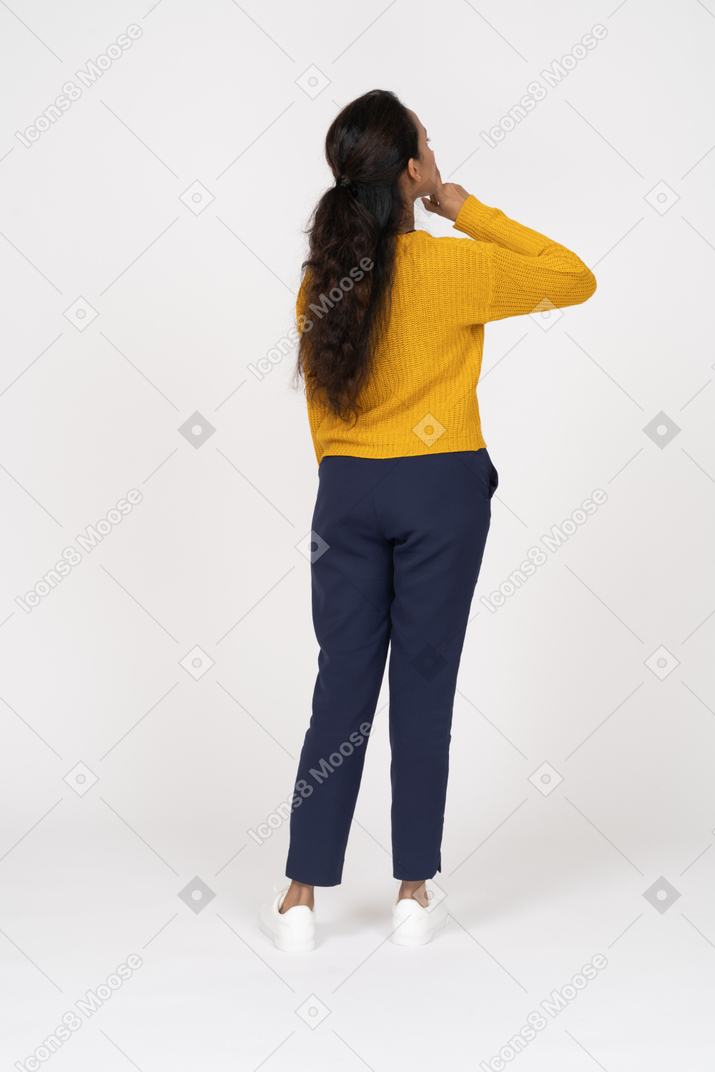 Вид сзади девушки в повседневной одежде, позирующей с рукой на подбородке