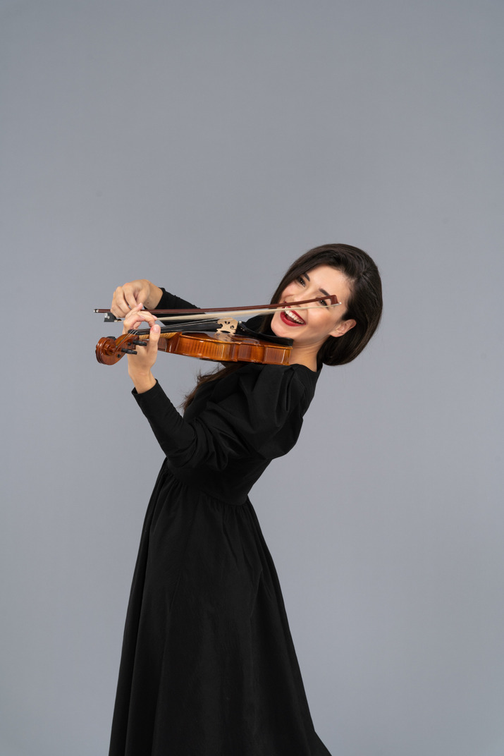 バイオリンを弾く黒いドレスを着た若い陽気な女性のクローズアップ