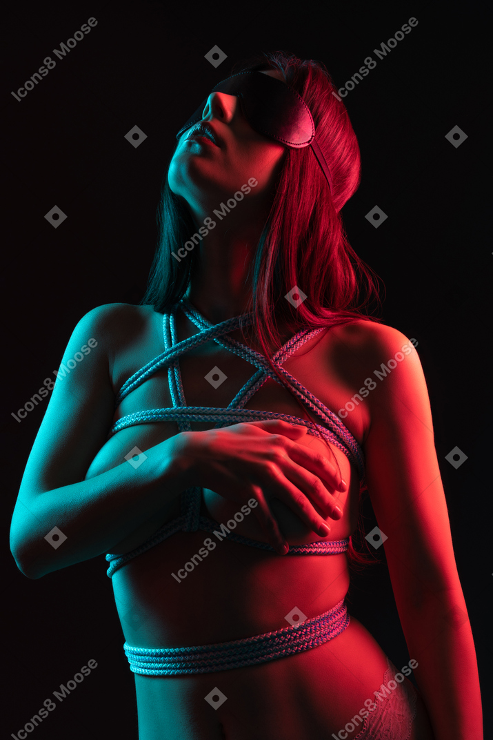 Close-up a male holding her chest standing in a blindfold under red-blue light