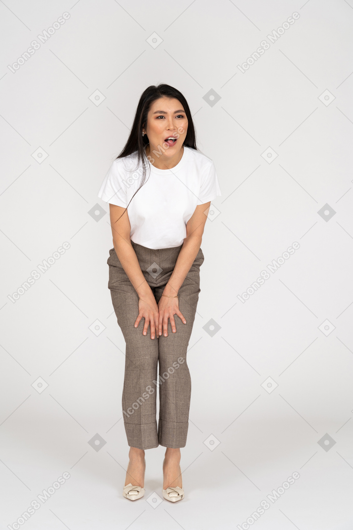 Vista frontal de una joven sorprendida en pantalones y camiseta inclinada