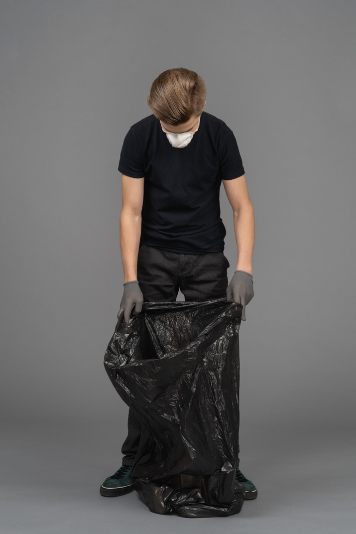 A young man wearing a mask and looking inside a trash bag