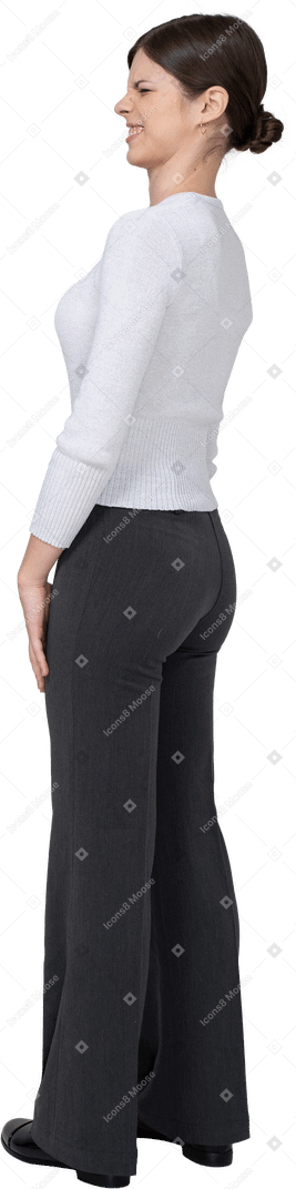 Three-quarter back view of a grimacing displeased young woman in office clothing
