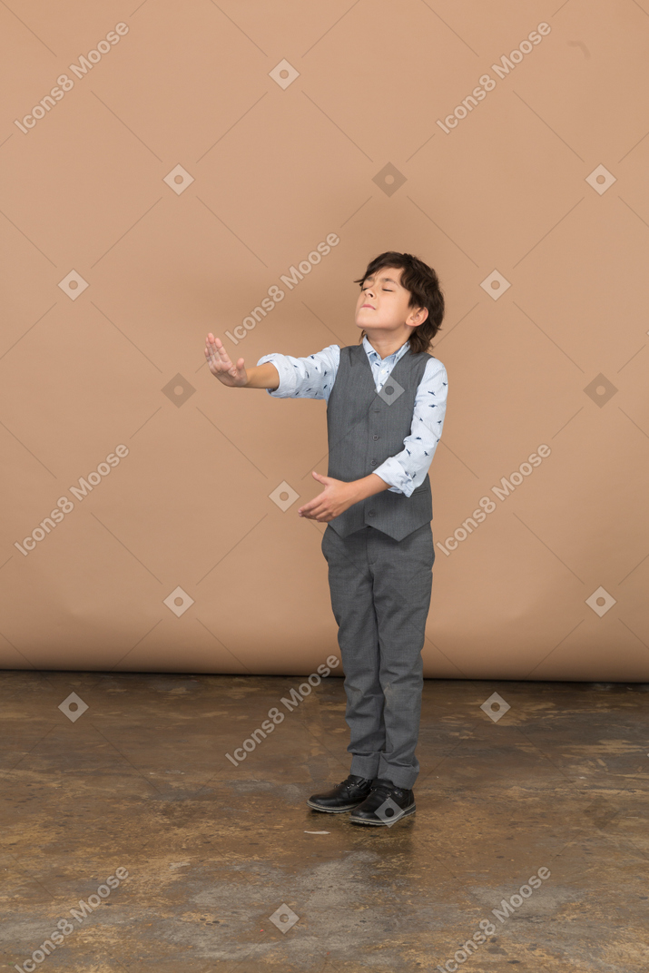 Vista frontale di un ragazzo carino in abito grigio in piedi con il braccio teso