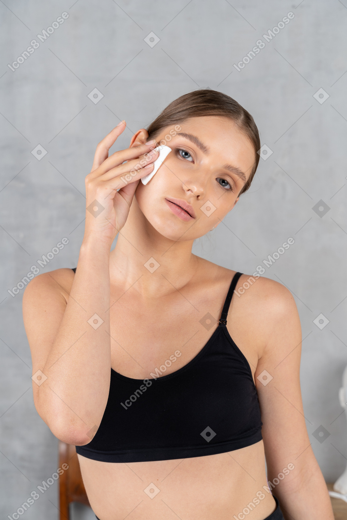 Young woman cleaning her face with cotton pad