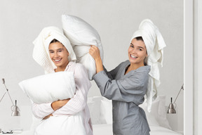 Two women with towels on their heads having a pillow fight